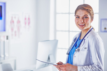 Young woman doctor is standing with board with clipboard smilin