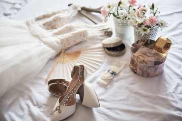 Fototapeta na wymiar Stylish white wedding bridal shoes, dress, perfume, flowers and jewelry.