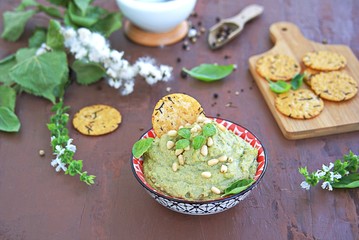 Green pea spread with almonds and basil on a brown concrete background. Decorated with pine nuts, served with crackers.
