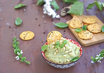 Green pea spread with almonds and basil on a brown concrete background. Decorated with pine nuts, served with crackers.
