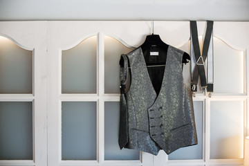 Groom's new waistcoat, tie and suspenders hanging on a hanger on a window.