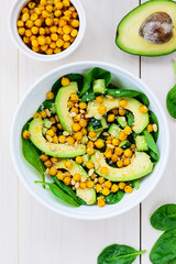 Salad from avocado, chickpea, spinach, cucumber and sesame on a white wooden table.