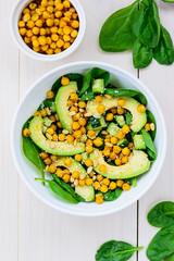 Salad from avocado, chickpea, spinach, cucumber and sesame on a white wooden table.