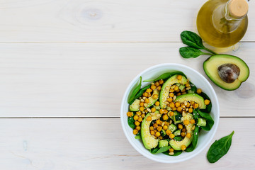 Salad from avocado, chickpea, spinach, cucumber and sesame on a white wooden table. Top view, copy space.
