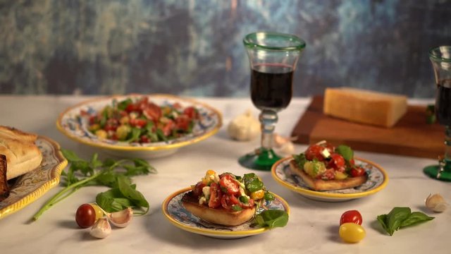 Turning shot to the right with blue background and focus on a serving of bruschetta with tomatoes, basil, and mozzarella cheese with professional lighting.