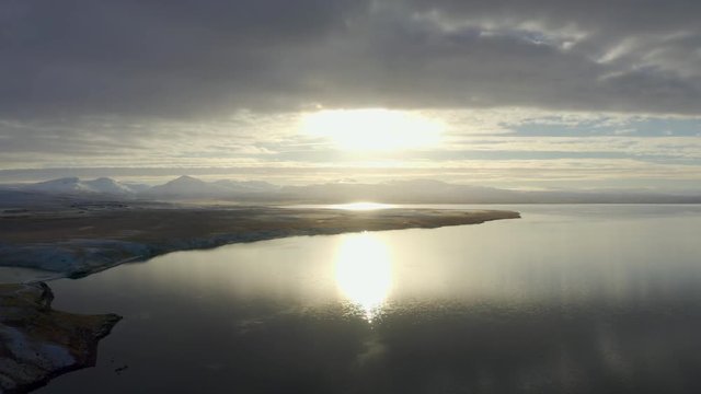 TRUCK RIGHT PAN LEFT: Drone establishes gorgeous sun setting over a lake in Iceland with mountain ranges on the horizon.