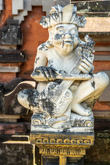 Klungkung, Bali, Indonesia - February 26, 2019: Closeup of white statue of violin player at Royal Palace. Black mold on statue and stone behind of red bricks.