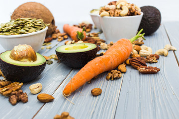 Healthy food and dieting concept. Focus on avocado and carrots. Nuts: cashews, almonds, pecans, walnuts, pumpkin seeds on a wooden table. Light summer flat lay food composition