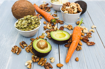 Healthy food and dieting concept. Avocado, carrots, nuts, cashews, almonds, pecans, walnuts, pumpkin seeds, coconut, grana padano hard cheese on a wooden table. Light summer food composition