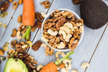 Healthy food and dieting concept. Focus on nuts: cashews, almonds, pecans, walnut. Avocado, carrots on a wooden table. Light summer food composition