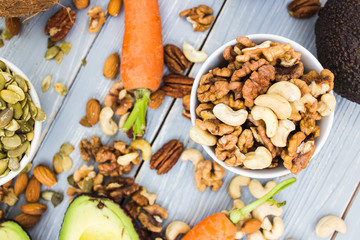 Healthy food and dieting concept. Focus on nuts: cashews, almonds, pecans, walnut. Avocado, carrots on a wooden table. Light summer food composition