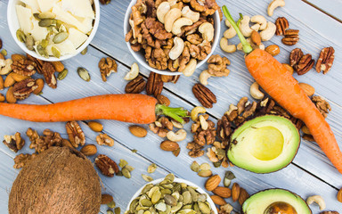 Healthy food and dieting concept. Avocado, carrots, nuts, cashews, almonds, pecans, walnuts, pumpkin seeds, coconut, grana padano hard cheese on a wooden table. Light summer food composition