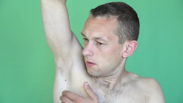 the young man sniffs his armpit, closes his nose. It smells bad. green background