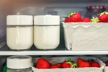 Refrigerator shelf with organic juicy strawberries in bio recycled paper boxes and homemade natural milk yogurt. Fridge filled with berries in cardboard containers. Healthy and eco friendly food diet
