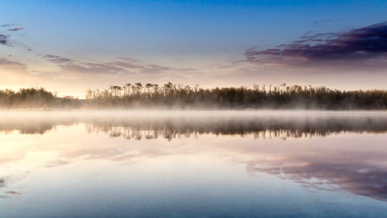 Fototapeta na wymiar Sunrise lake and sky mirrored images, Calm as glass lake water reflecting the sky above, misty water