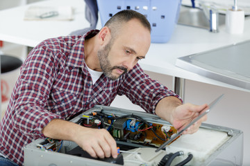 mature serviceman working on appliance and holding tablet