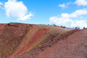 Tourists standing on the edge of Silvestri craters on Mount Etna in Italian Sicily. The colorful volcanic landscape is popular with hikers