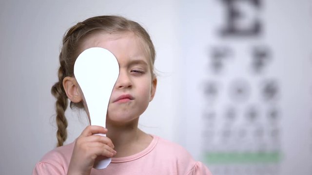 Female preschooler closing eye for complete vision exam, diagnostics of sight