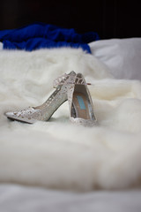 a tiara sits on a pair of beautiful sequined silver bridal shoes against white fur on wedding day 	