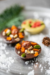 Fototapeta na wymiar Christmas theme. Handmade chocolates candy. Mini chocolate dessert covered with nuts and dried fruits. Garland lamps bokeh on background. Copy space