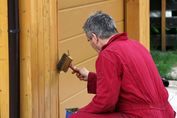 Ein Mann streicht mit einer Holzschutzfarbe  eine Garage