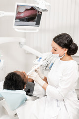 Obraz premium Inspection with a dental macro camera and displays the result on the monitor. Young woman dentist treating root canals in the dental clinic. Man patient lying on dentist chair with open mouth.