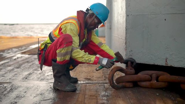 Seaman AB or Bosun on deck of vessel or ship , wearing PPE personal protective equipment - helmet, coverall, lifejacket, goggles. He works with gob chain