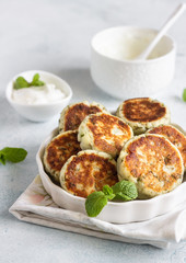 Cottage cheese fritters (syrniki) with green pea, dill, mint and sauce. Light stone background. Healthy breakfast or diet lunch. Copy space.