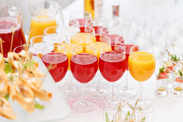 Table top full of glasses Glasses not alcoholic drinks, orange juice, water and berry juice. s with canapes and antipasti in the background.