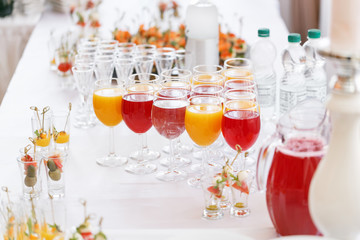 Table top full of glasses Glasses not alcoholic drinks, orange juice, water and berry juice. s with canapes and antipasti in the background.