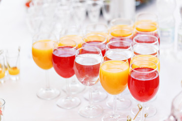 Table top full of glasses Glasses not alcoholic drinks, orange juice, water and berry juice. s with canapes and antipasti in the background.