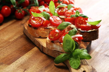 Traditional italian antipasto bruschetta appetizer with cherry tomatoes, cream cheese, basil leaves and balsamic vinegar on cutting board. Antipasti