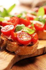 Traditional italian antipasto bruschetta appetizer with cherry tomatoes, cream cheese, basil leaves and balsamic vinegar on cutting board. Antipasti