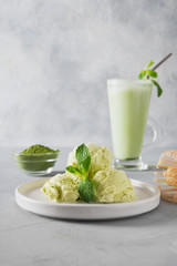 Green matcha ice cream and tea in latte glass on grey table.