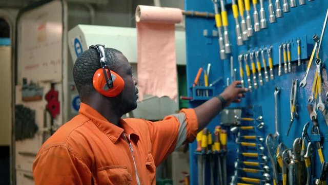 African marine engineer officer in engine control room ECR. He works in workshop and chooses correct tools and equipment