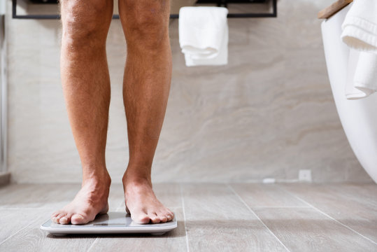 Close up of the man being barefooted in bathroom and using scales