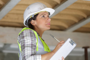 Fototapeta premium female builder in safety vest and hardhat writing in clipboard