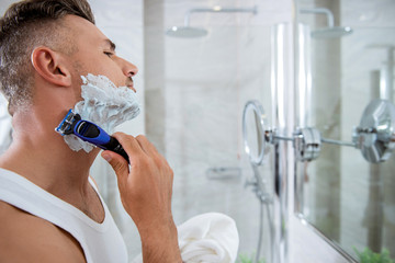 Concentrated man shaving his face and looking at the mirror