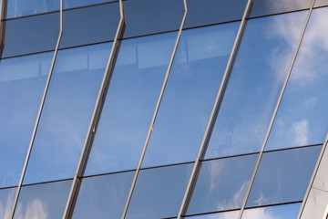 closeup of a modern window glass building with blue sky and clouds reflecting in it