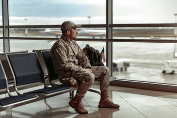 American soldier in camouflage sitting near window and looking through it
