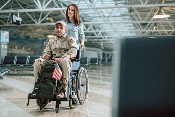 Fototapeta na wymiar Wife carrying wheelchair and situating behind her husband in military uniform