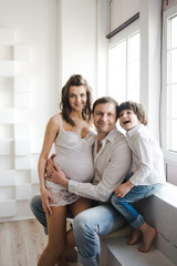 Happy family waiting for a second child. Pregnant woman with husband and little boy . Second pregnancy, maternity concept. Happy family near the window. White background.