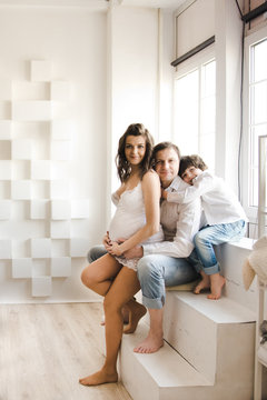 Happy family waiting for a second child. Pregnant woman with husband and little boy . Second pregnancy, maternity concept. Happy family near the window. White background.