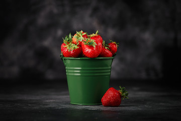 Strawberries in a bucket on the dark concrete background