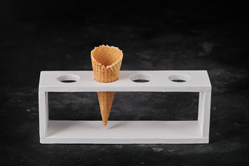 single empty waffle cone in wood holder dark concrete background