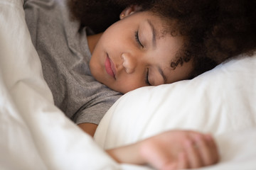 Cute little african american kid girl sleeping alone in bed