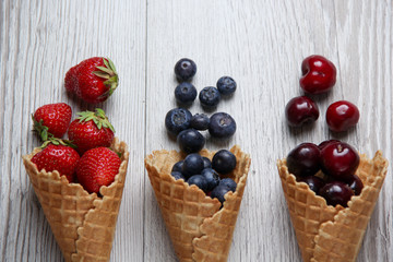 Summer fresh organic berries, cherries, strawberies and blueberries in waffle cones on white wooden background. Space for text