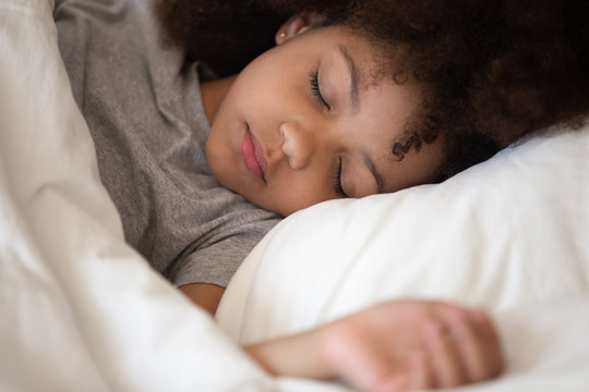 Cute little african american kid girl sleeping alone in bed