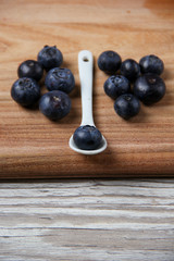 Fresh organic blueberry on a white ceramic spoon at wooden board and other blueberries near.
