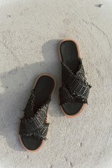 black wicker shoes with flat sole. Stylish summer slates without legs. Fashionable female slippers on gray asphalt with a shadow on it.